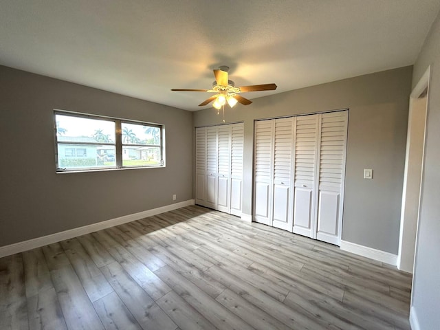 unfurnished bedroom with baseboards, light wood-type flooring, a ceiling fan, and multiple closets