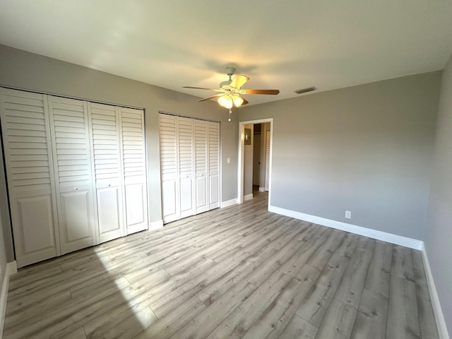 unfurnished bedroom with ceiling fan, light wood-style flooring, visible vents, baseboards, and multiple closets