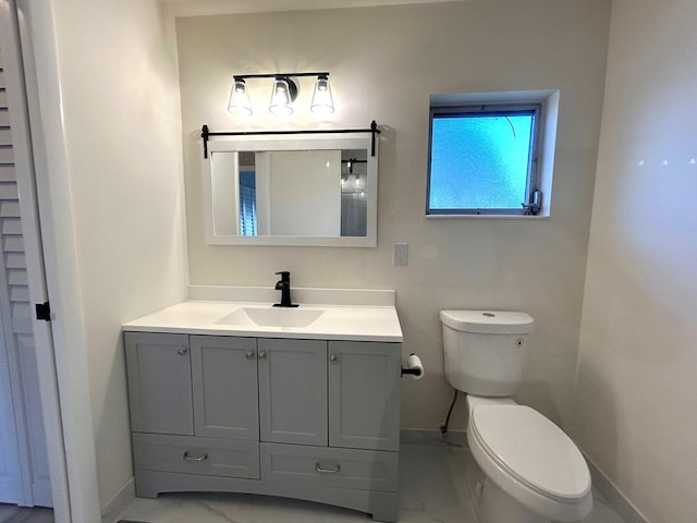 half bathroom featuring toilet, marble finish floor, vanity, and baseboards