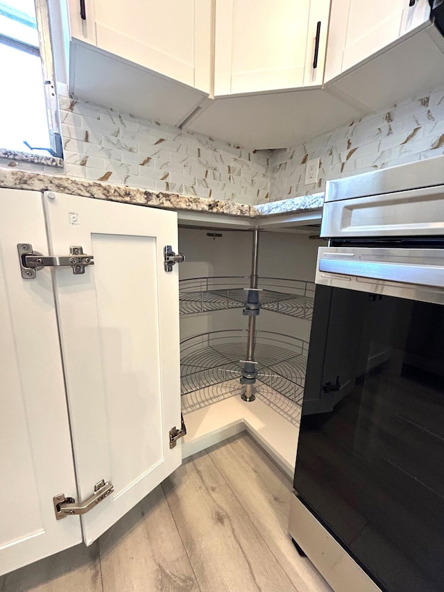 interior space featuring wall oven, white cabinets, light wood-style flooring, and light stone counters