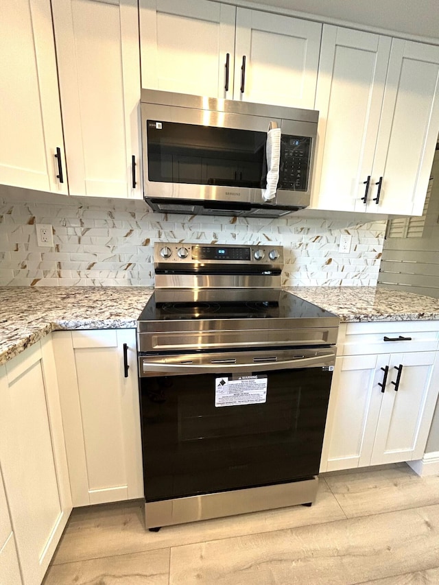 kitchen with appliances with stainless steel finishes, white cabinetry, and light stone counters