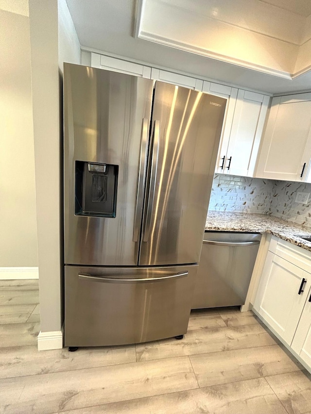 kitchen with stainless steel appliances, light wood-style floors, white cabinets, backsplash, and light stone countertops