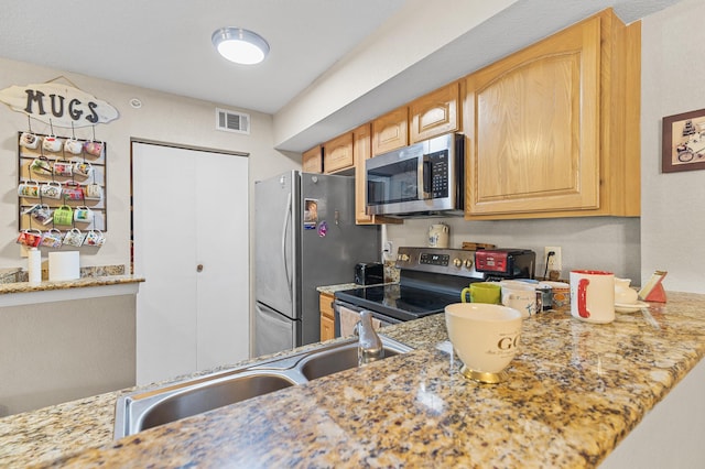 kitchen featuring stainless steel appliances, visible vents, light brown cabinets, a sink, and light stone countertops