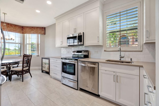 kitchen featuring a notable chandelier, stainless steel appliances, decorative backsplash, a sink, and plenty of natural light