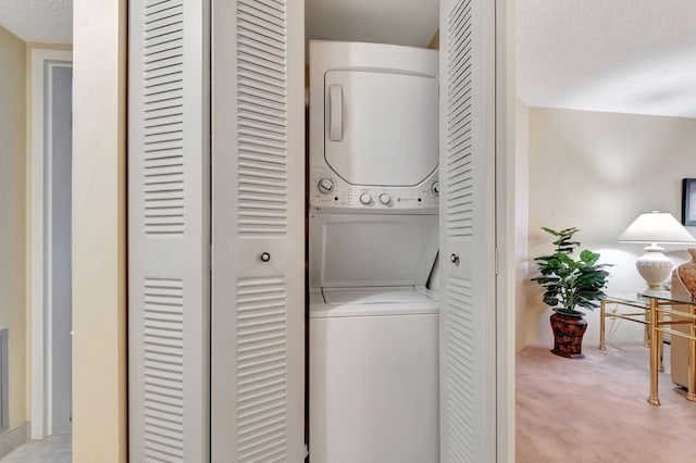 laundry room featuring stacked washer / dryer, laundry area, light colored carpet, and a textured ceiling