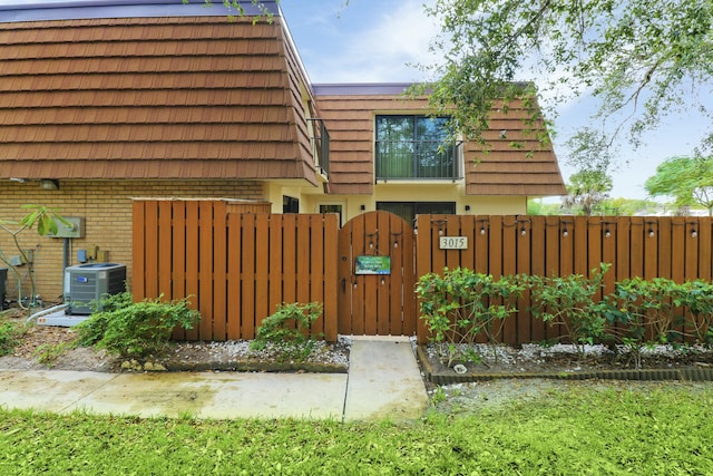 view of front of property featuring mansard roof, a gate, fence, central air condition unit, and brick siding