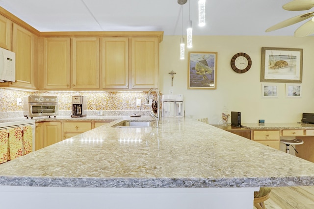 kitchen with a peninsula, light brown cabinetry, a sink, and decorative backsplash