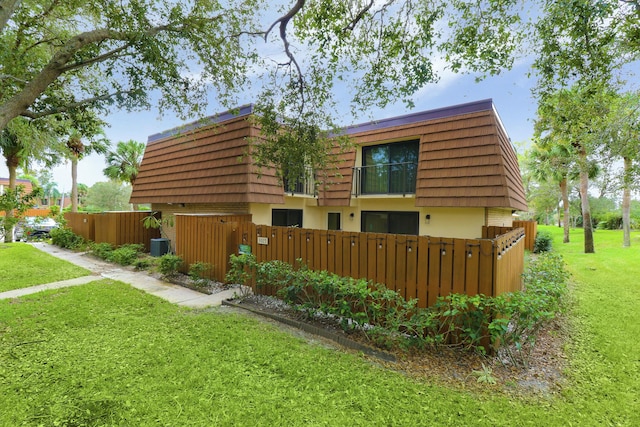 view of side of home featuring a fenced front yard, a yard, and mansard roof