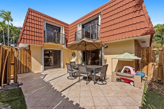 back of house featuring mansard roof, a balcony, a tiled roof, outdoor dining area, and stucco siding