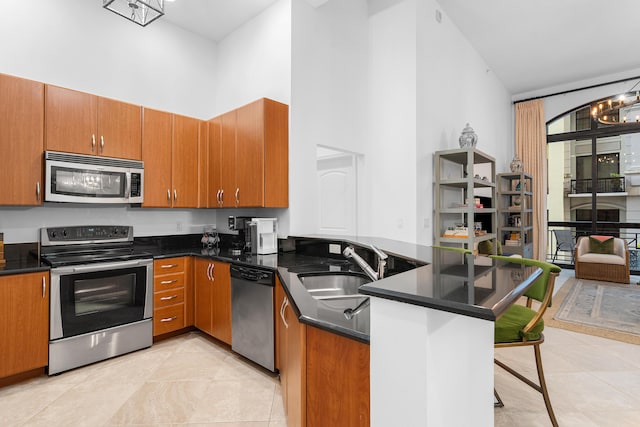 kitchen with brown cabinetry, appliances with stainless steel finishes, high vaulted ceiling, a chandelier, and a sink