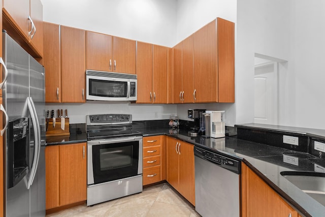 kitchen with dark stone counters, appliances with stainless steel finishes, brown cabinetry, and light tile patterned floors