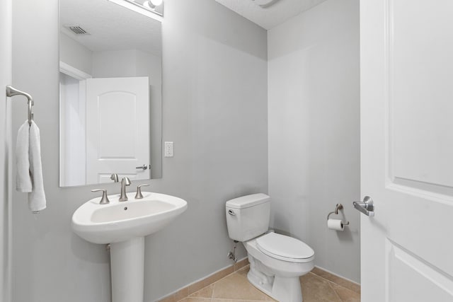 bathroom featuring baseboards, visible vents, toilet, tile patterned floors, and a textured ceiling