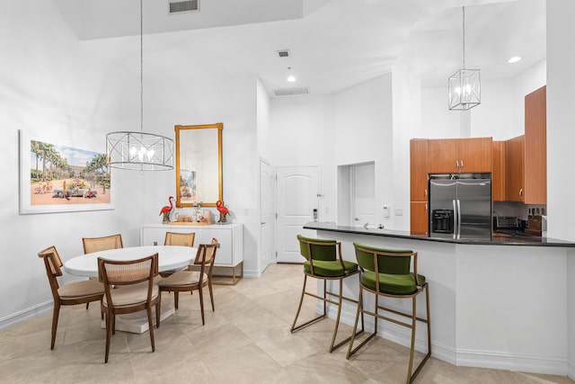 kitchen with dark countertops, hanging light fixtures, a towering ceiling, brown cabinetry, and stainless steel fridge with ice dispenser