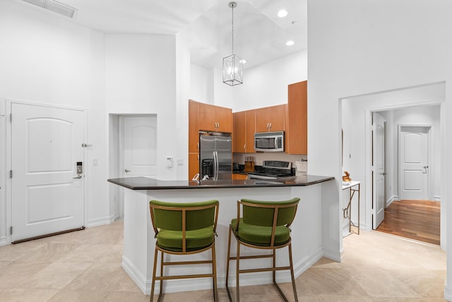 kitchen featuring decorative light fixtures, dark countertops, a towering ceiling, appliances with stainless steel finishes, and a peninsula