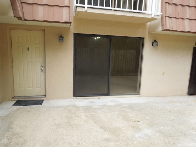 view of exterior entry with a patio, a tiled roof, a balcony, and stucco siding