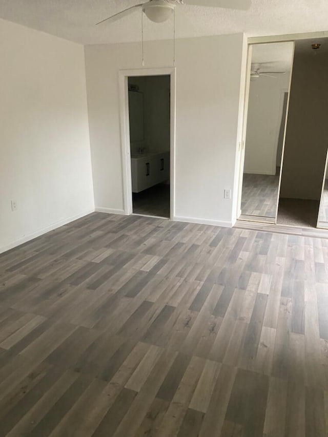 unfurnished bedroom featuring baseboards, ensuite bath, ceiling fan, wood finished floors, and a closet