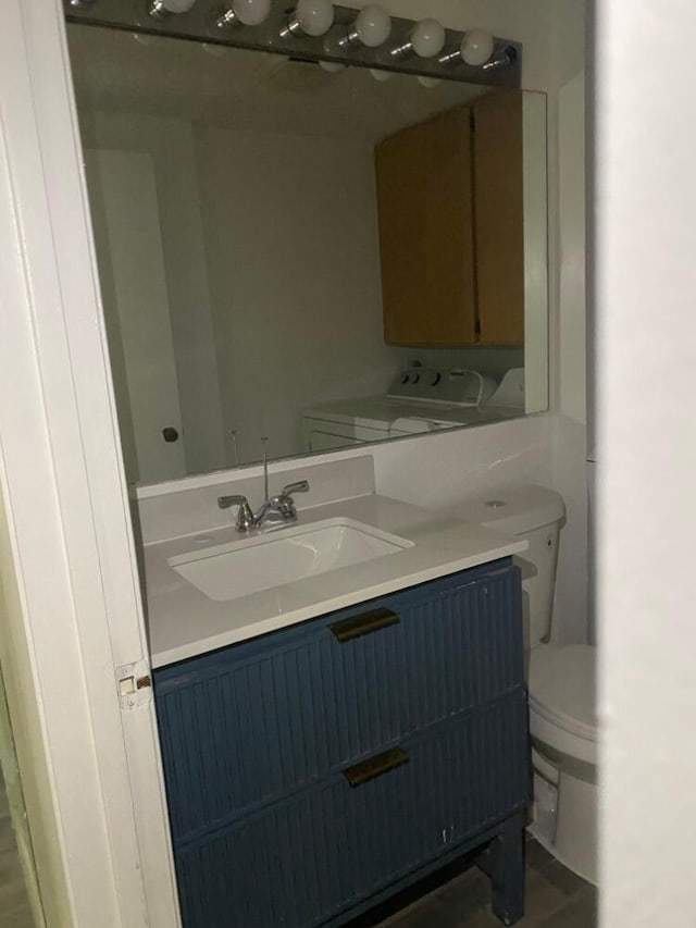 half bathroom with toilet, washing machine and clothes dryer, and vanity