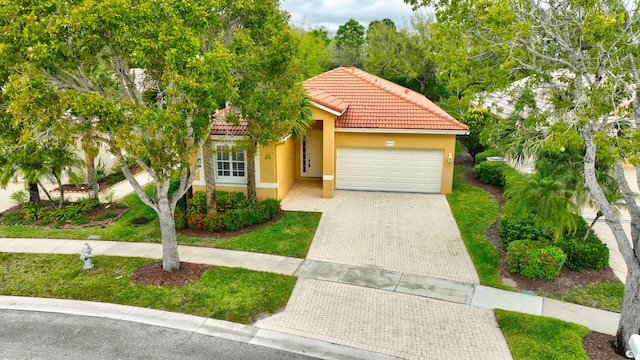 mediterranean / spanish-style house featuring decorative driveway, a tile roof, an attached garage, and stucco siding