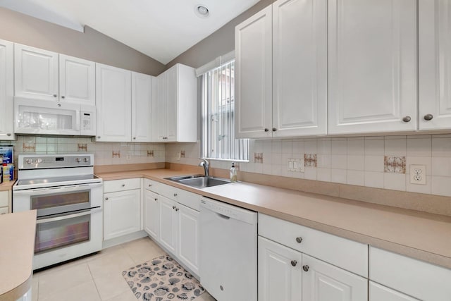 kitchen featuring light tile patterned flooring, white appliances, a sink, white cabinets, and vaulted ceiling