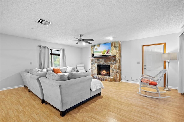 living area with baseboards, visible vents, a textured ceiling, light wood-style floors, and a fireplace