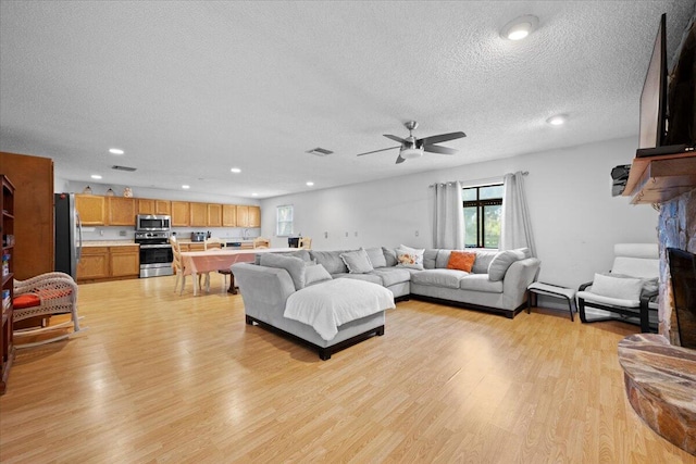 living area with light wood-type flooring, visible vents, a stone fireplace, and a textured ceiling