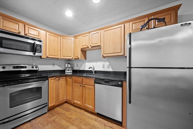 kitchen featuring appliances with stainless steel finishes, dark stone countertops, a textured ceiling, light wood-style floors, and a sink