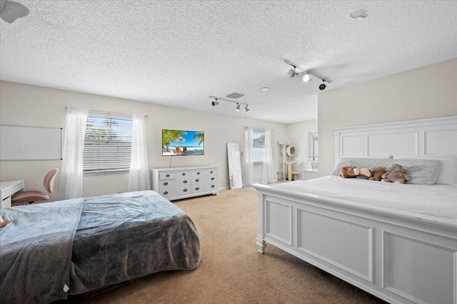 carpeted bedroom with a textured ceiling, visible vents, and track lighting