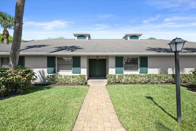 ranch-style home featuring roof with shingles, a front yard, and stucco siding