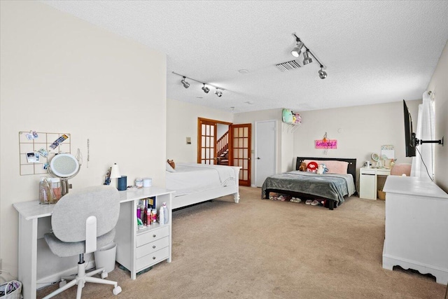 bedroom featuring visible vents, light colored carpet, a textured ceiling, and rail lighting