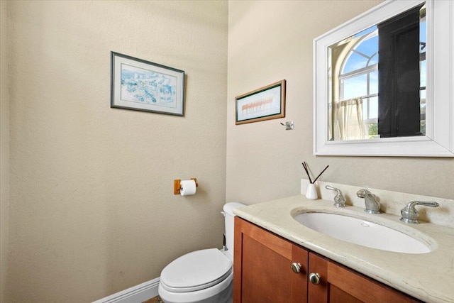 half bath with baseboards, vanity, and toilet