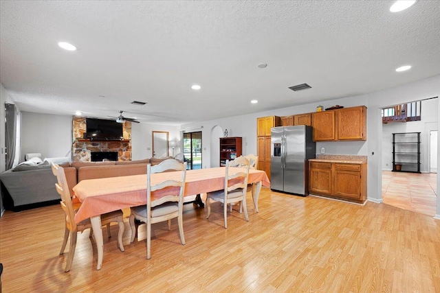 dining room with recessed lighting, visible vents, a stone fireplace, a textured ceiling, and light wood-type flooring