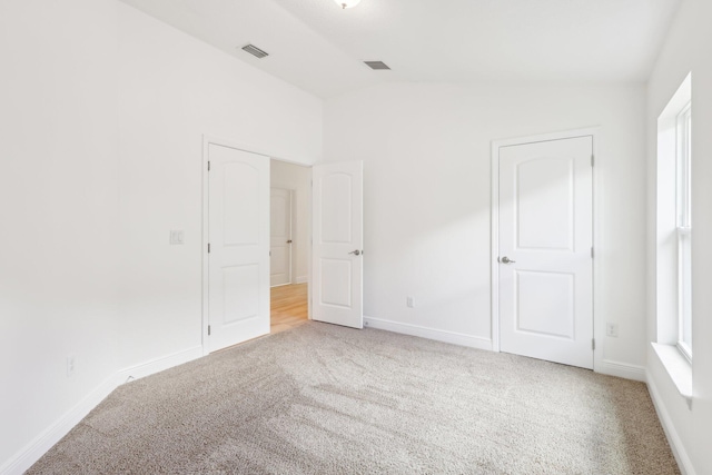 unfurnished bedroom with lofted ceiling, carpet, visible vents, and baseboards