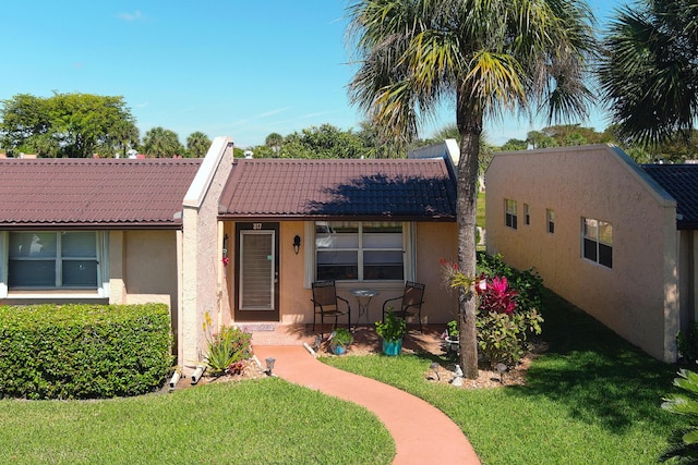 ranch-style home with a tiled roof, a front yard, and stucco siding