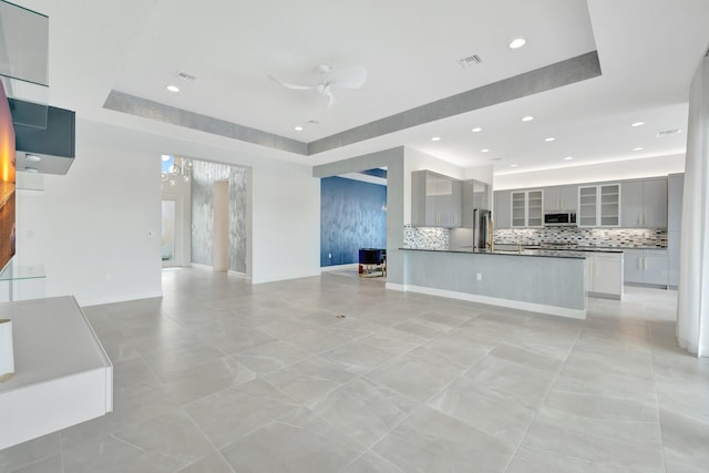 unfurnished living room with recessed lighting, a raised ceiling, visible vents, a ceiling fan, and baseboards