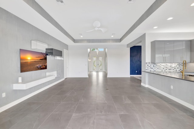 unfurnished living room featuring baseboards, a raised ceiling, a sink, and french doors