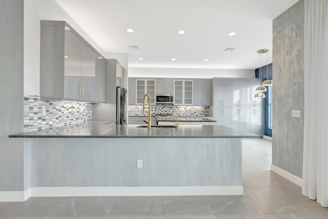 kitchen with stainless steel appliances, decorative backsplash, gray cabinetry, dark stone counters, and a peninsula