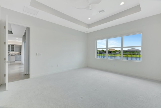 unfurnished room with baseboards, a tray ceiling, and light colored carpet