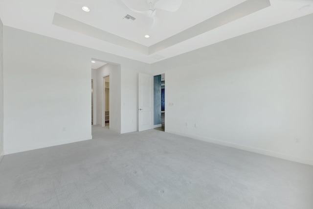 spare room with a tray ceiling, visible vents, and baseboards