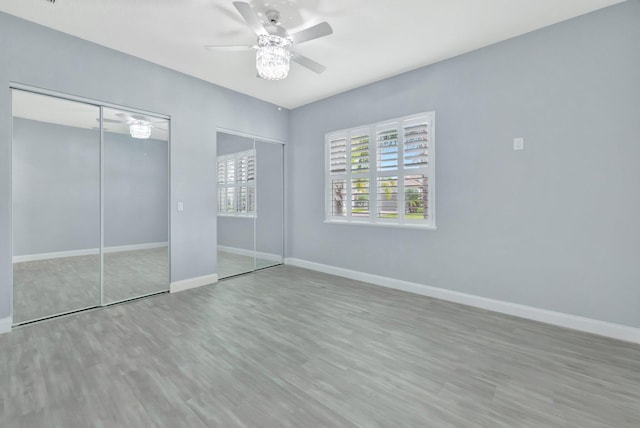 unfurnished bedroom with ceiling fan, baseboards, multiple closets, and wood finished floors