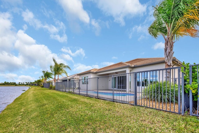 back of house featuring a water view, fence, a lawn, a fenced in pool, and stucco siding