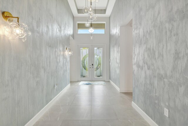 tiled foyer entrance with a towering ceiling, baseboards, a tray ceiling, and french doors