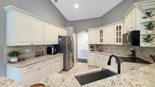 kitchen with arched walkways, a sink, freestanding refrigerator, open shelves, and glass insert cabinets