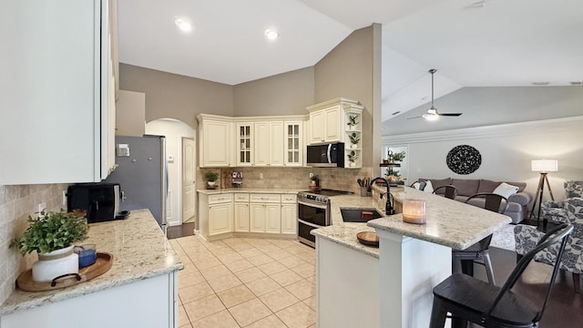 kitchen featuring light stone counters, a breakfast bar, appliances with stainless steel finishes, glass insert cabinets, and a peninsula