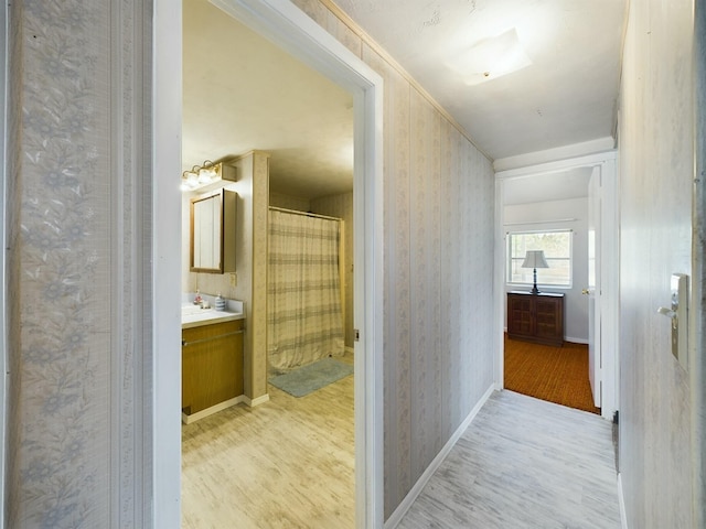 hallway with light wood-style floors, baseboards, and wallpapered walls