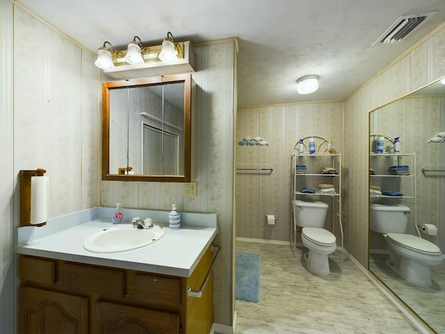 half bathroom with wallpapered walls, baseboards, visible vents, toilet, and vanity