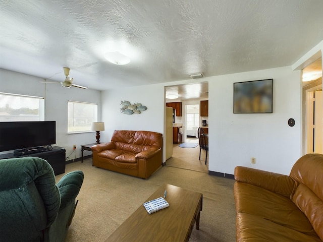 carpeted living area with a textured ceiling, ceiling fan, visible vents, and baseboards