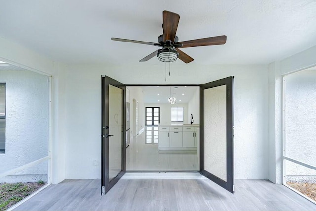 interior space with light wood-type flooring, a ceiling fan, and a textured wall