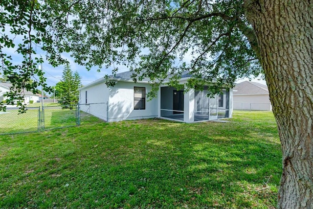 back of property featuring a lawn, a sunroom, a gate, fence, and stucco siding