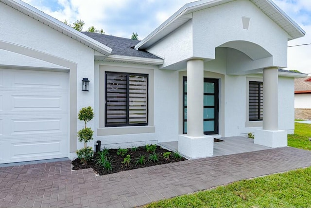 doorway to property featuring an attached garage, roof with shingles, and stucco siding