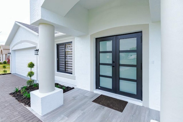 view of exterior entry with a garage, french doors, decorative driveway, and stucco siding